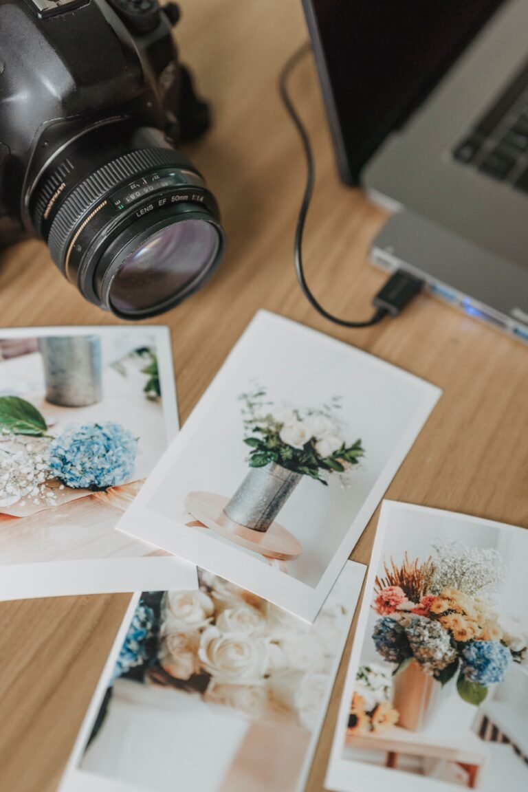 From above abundance of printed images placed on wooden table with professional photo camera and modern laptop in light room