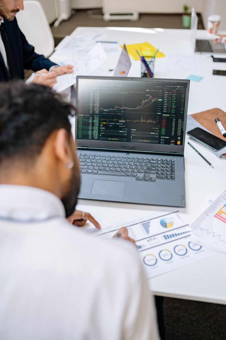 Business professionals analyzing stock charts and graphs on a laptop in an office setting.